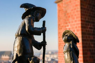 Polonya, Wroclaw 'da iki bronz cüce heykel, kırmızı tuğla bir yapıya ve sıcak aydınlatmada bulanık bir şehir manzarasına karşı kurulmuş..