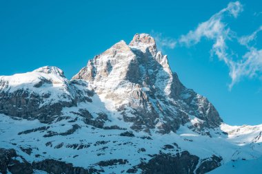 İsviçre 'nin Zermatt kenti yakınlarındaki ikonik Matterhorn dağı, arkasında engebeli yamaçlar ve berrak mavi gökyüzü bulunan güneş ışığı altında karla kaplıdır..