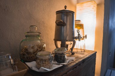 İçi ahşap bir masa, metal bir içecek kutusu, kurutulmuş elma dilimleri, atıştırmalık kavanozları ve sıcak ışıkta parlayan bir lamba..