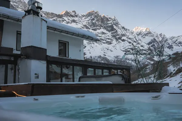 Zermatt, İsviçre 'de kar kaplı modern bir otel, ön planda jakuzisi, kayak asansörü yapıları ve yumuşak doğal ışık altında Alpler..