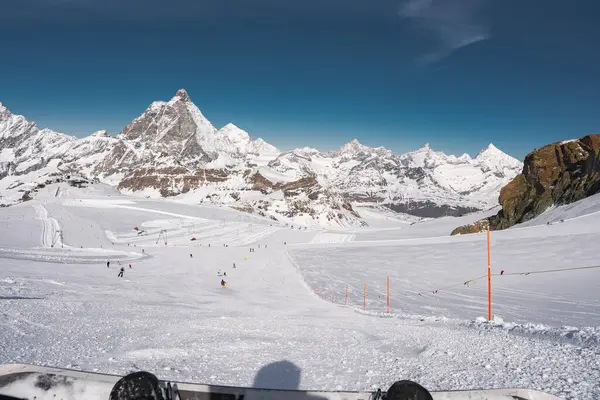 İsviçre 'deki Zermatt kayak merkezi manzarası. Matterhorn, kar kaplı yamaçlar, kayakçılar, kayak asansörleri ve ön planda bir snowboard..