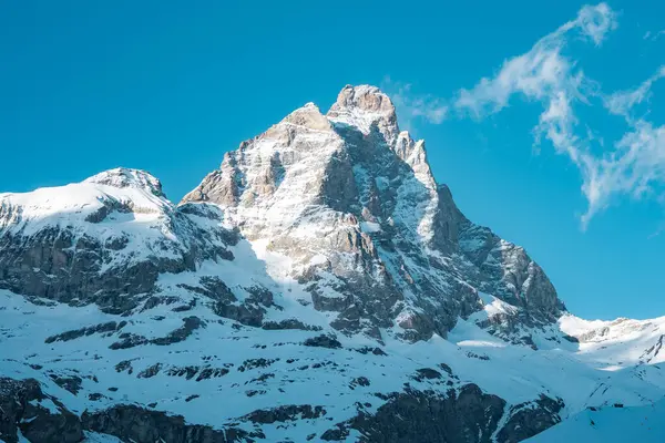 İsviçre 'nin Zermatt kenti yakınlarındaki ikonik Matterhorn dağı, arkasında engebeli yamaçlar ve berrak mavi gökyüzü bulunan güneş ışığı altında karla kaplıdır..