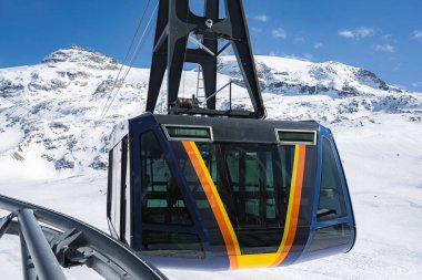 İsviçre 'nin Zermatt kentindeki kar kaplı dağlarda açık mavi gökyüzünün altında sarı ve kırmızı çizgili parlak bir teleferik..
