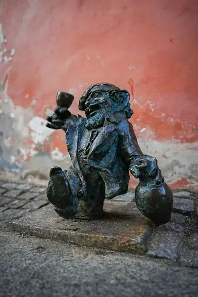 Polonya 'nın Wroclaw kentindeki küçük bir bronz cüce heykeli, kırmızı bir duvarın yanında kaldırım taşlarının üzerinde duruyor, elinde neşeli bir vaziyette bir kadeh ve çuval tutuyor..