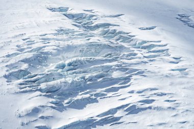 İsviçre, Zermatt yakınlarındaki bir buzulda derin yarıklar, sıkıştırılmış buz tabakaları ve etrafındaki karla çelişen mavimsi renkler bulunur..