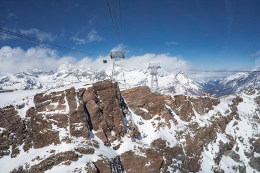 İsviçre 'nin Zermatt şehrinde engebeli zirveleri, kayak kaldırma kabloları ve karla kaplı arazisi açık mavi bir gökyüzünün altında..