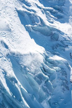 İsviçre 'nin Zermatt kentindeki bir buzulun hava perspektifi, karmaşık yarıklar, pürüzsüz buz oluşumları ve zıt beyaz ve mavi tonlarda.