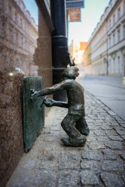 Küçük bir bronz cüce heykeli, arka planda tarihi binalar bulunan Wroclaws eski kasabasındaki kaldırımda dikdörtgen bir nesneyi itiyor..