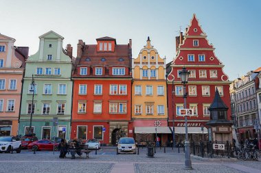 Süslü gablonlar, ahşap bir büfe, kaldırım taşı meydanı, park edilmiş arabalar, bisikletler ve Wroclaw, Polonya 'daki insanlarla dolu renkli cepheler..