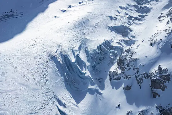 İsviçre 'nin Zermatt kentindeki bir buzulun hava manzarasında engebeli buz oluşumları, yarıklar, sivri kayalar ve çevre tepelerden gelen gölgeler yer alıyor..