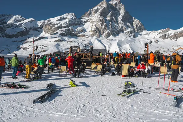 Kayakçılar ve ziyaretçiler arka planda Matterhorn olan ahşap bir oturma alanının yakınında toplanıyorlar. Kar yamaçları ve kayak ekipmanları Alp ayarı tamamlandı.