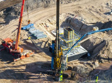 Riga, Letonya 'da aktif inşaat alanında kırmızı bir vinç, sondaj makinesi, iskele, güçlendirilmiş beton yapı ve güvenlik donanımı olan işçiler bulunuyor..