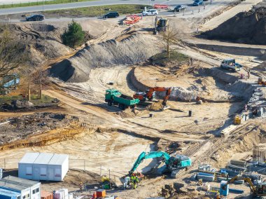 Riga, Letonya 'daki aktif inşaat alanı, ağır makineler, işçiler, kısmen inşa edilmiş döner kavşak ve kumlu arazide geçici yapılar gösteriyor..