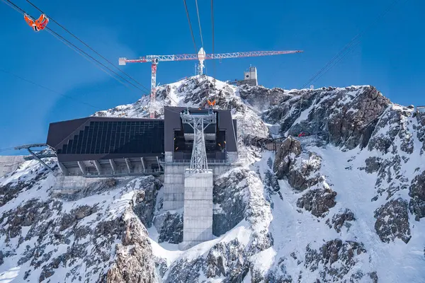 İsviçre 'nin Zermatt kentindeki karlı bir dağda, üzerinde siyah paneller ve beton destekli gösterişli bir kayak kaldırma istasyonu faaliyet gösteren kırmızı bir teleferiği var..