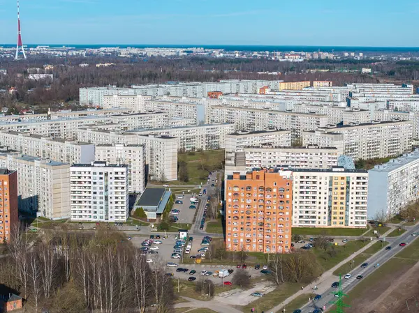 Riga, Letonya 'daki Sovyet döneminden kalma apartman blokları turuncu tuğlalı bir bina, otoparklar, yeşil alanlar ve Riga TV kulesi görünür..