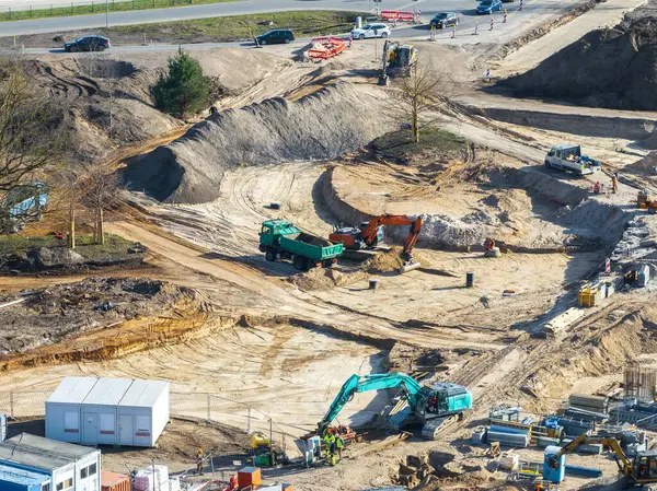 Riga, Letonya 'daki aktif inşaat alanı, ağır makineler, işçiler, kısmen inşa edilmiş döner kavşak ve kumlu arazide geçici yapılar gösteriyor..