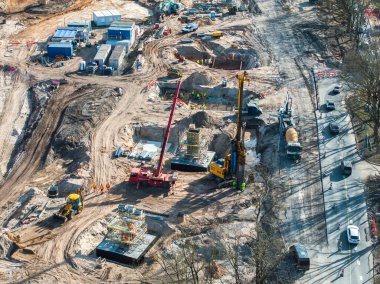 Riga, Letonya 'daki büyük inşaat sahasında vinçler, kazıcılar, güvenlik ekipmanları, kazı çukurları ve hafif trafiği olan yakındaki karayolu çalışanları yer alıyor..