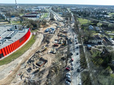 Riga, Letonya 'da vinçleri, kazıcıları ve malzemeleri olan büyük bir inşaat alanı. Kırmızı kıvrımlı bir bina, işlek bir yol ve yerleşim alanları görülebilir..