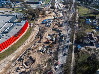 Riga, Letonya 'da geniş bir inşaat alanı, arka planda ağır makineler, kırmızı bir bina, temizlenmiş arazi, siperler ve yerleşim alanları yer alıyor..