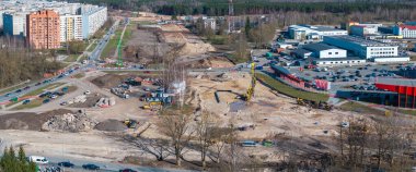 Riga, Letonya 'da büyük bir inşaat alanı, ağır makineler, inşaat halindeki bir döner kavşak, kentsel binalar, ve orman geçmişi.