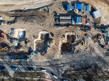 Riga, Letonya 'daki bir inşaat alanının hava görüntüsü vinçleri, makineleri, kazı alanlarını, mavi çatılı yapıları ve yakındaki araçlı kentsel yolları gösteriyor..