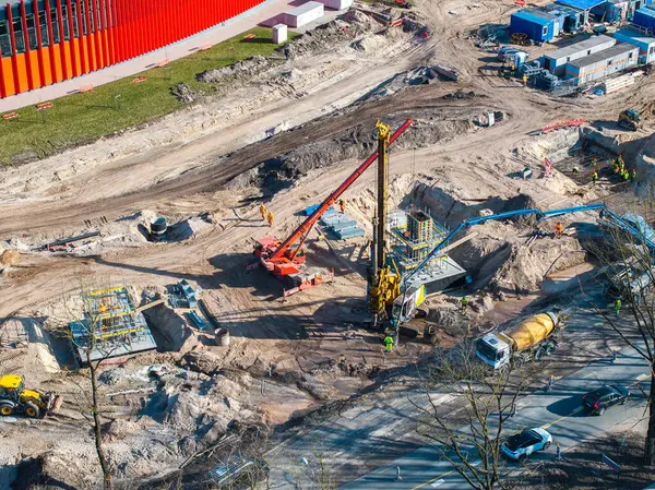 Riga, Letonya 'da aktif inşaat alanı, vinçler, çimento karıştırıcı, yüksek görüş mesafesi olan işçiler, ve arka planda modern kırmızı bir bina..