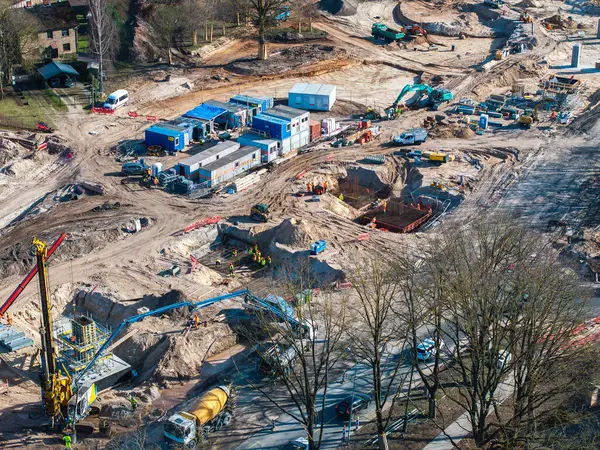 Riga, Letonya 'daki inşaat alanında kazıcılar, vinçler, işçiler ve taşınabilir binalar görülüyor. Kentin çevresini çevreleyen ağaçlar ve binalar.