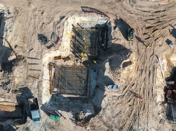 Riga, Letonya 'da bir inşaat alanının havadan görünüşü, beton temeller, yüksek görüş mesafesi kıyafetleri, makineler ve güvenlik bariyerleri olan işçiler.