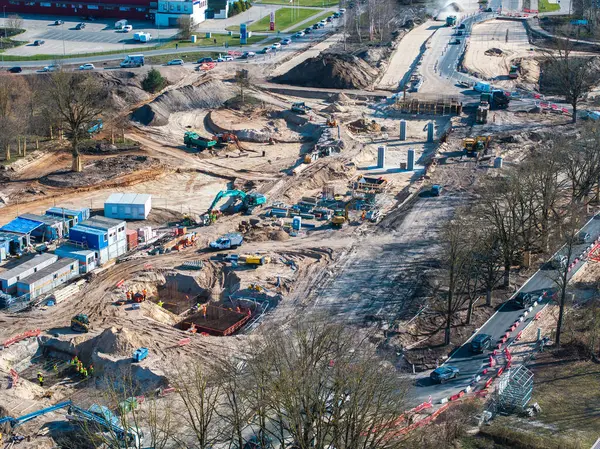Riga, Letonya 'daki büyük inşaat sahasında ağır makineler, yol çalışması, beton sütunlar ve kentsel bir ortamda yoğun bir yol bulunuyor..