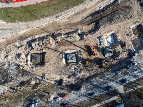Riga, Letonya 'daki bir inşaat alanının hava görüntüsü vinçleri, kazıcıları, beton temelleri, eğri toprak bir yol ve yakınlardaki kırmızı bir binayı gösteriyor..