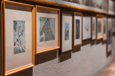 Ahşap çerçeveler bir galeri duvarında dağ manzaraları ve dağlık manzaralar sergiler. Sıcak ışıklandırma, iç otel ortamındaki dokuları geliştirir..