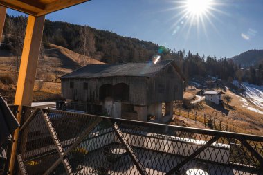 Yıpranmış çatısı olan, kırsal ahşap bir ahır, İtalya 'nın Güney Tyrol kentinde, kayan tepeler ve bir ormanın yanında duruyor. Modern bir balkon karlı manzaraya bakıyor..