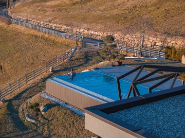 Güney Tyrol, İtalya 'da çağdaş bir otel. Yükseltilmiş sonsuz havuzu, parlak tasarımı, yuvarlanan tepeleri, ahşap çitleri ve arka planda seyrek ağaçları var..