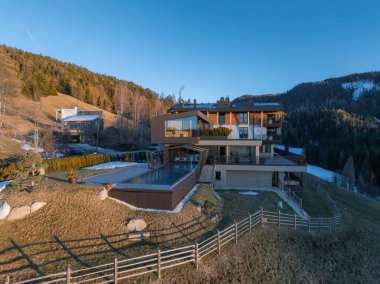 Camdan pencereleri, terasları ve sonsuz havuzu olan çağdaş bir otel tepeler, seyrek ağaçlar, kar bantları ve Güney Tyrol 'daki dağ manzaralarıyla çevrili..
