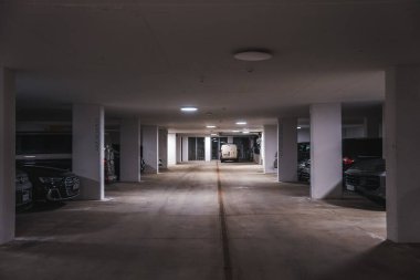 Beyaz beton sütunları, bej zemini, lüks arabaları, tavan lambaları ve İtalyan Alpleri 'nin çıkışına yakın beyaz bir minibüsü olan temiz yeraltı otoparkı..