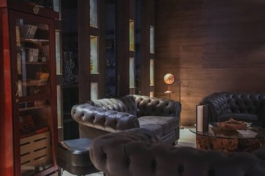 Koyu deri koltukları, cam bir sehpası, tahta panelli duvarları ve İtalyan Alpleri 'ndeki lüks bir otelde sıcak ışıklandırması olan bir salon..