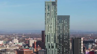 Manchester, İngiltere 'nin hava görüntüsü, Deansgate Meydanı gökdelenini, modern ve tarihi binaları, vinçleri ve açık bir gökyüzünün altındaki uzak tepeleri vurguluyor.