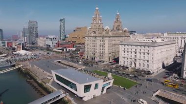 Liverpool 'un sahil manzarasında Kraliyet Liver Binası, Liverpool Müzesi ve Mersey Nehri boyunca hareket eden bir feribot var..