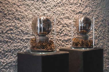 Taş kaidedeki iki cam kap, lüks bir otelin iç kısımlarında dokulu bir duvara dayanan metalik küreler ve altın kozalaklar içeriyor..