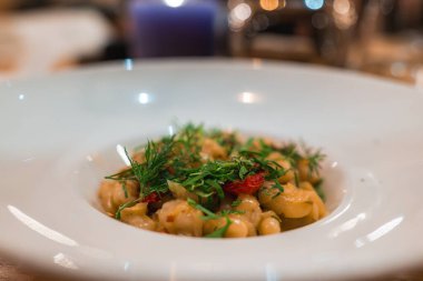 Dereotlu, maydanozlu ve kırmızı biberli makarnayı beyaz kaseye koy. Sıcak bir ışık ve mor bir mum rahat bir atmosfer yaratır..