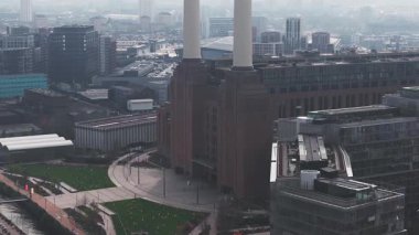 Londra 'daki Thames Nehri' nin havadan görünüşü hareketli bir tekne, modern binalar, endüstriyel yapılar ve ziyaretçi ve patikaların olduğu yeşil bir park..