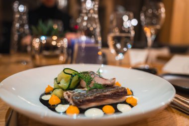 Dereotu, portakal ve beyaz sosla süslenmiş kurutulmuş balık filetosu ve soslu salatalık kurdelesi lüks bir İtalyan Alpleri restoranında zarif bir masada..