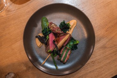 Kurutulmuş et dilimleri, sotelenmiş sebzeler, portakal sosu, çam fıstığı ve ahşap bir masada seramik tabakta çıtır çıtır bir garnitür içeren bir tabak..