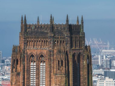 Liverpool Katedrali 'nin Gotik Diriliş mimarisi sivri kemerler ve kulelerle göze çarpıyor, vinçleri ve açık mavi gökyüzü olan bir şehir manzarasına karşı..
