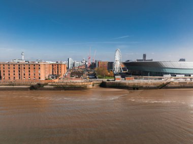 Albert Dock 'un kırmızı tuğla depolarının, MandS Bank Arena' nın, Liverpool Çarkıfeleğinin ve açık mavi gökyüzünün altındaki Mersey Nehri 'nin havadan görünüşü..