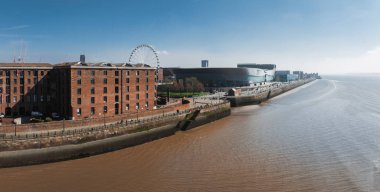 Liverpool 'un hava görüntülerinde Albert Rıhtımı kırmızı tuğla depoları, Liverpool Tekerleği, MandS Bank Arena ve Mersey Nehri berrak bir gökyüzü altında.
