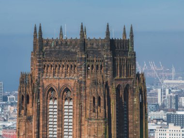 Liverpool Katedralleri Gotik Diriliş mimarisi sivri kemerler ve kulelerle göze çarpıyor, vinçleri ve açık mavi gökyüzü olan bir şehir manzarasına karşı..
