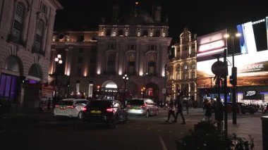 Gece Londra 'da Piccadilly Sirki' nde ışıklı reklam panoları, yayalar, hareket halindeki arabalar ve kırmızı çift katlı otobüsler vardı..