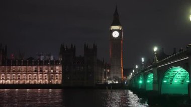 Büyük Ben ve Westminster Sarayı 'nın durağan gece sahnesinde Thames Nehri kıyısında Westminster Köprüsü ve parlayan sokak lambaları görünür..