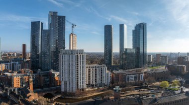 Manchester, İngiltere 'nin hava manzarası, modern gökdelenler, bir inşaat vinci, Irwell Nehri ve açık mavi gökyüzü altında tarihi tuğla binalar..